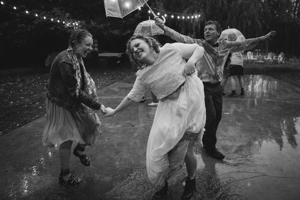 Black and white photo of a bride and friends dancing in the rain, photo by Jenny Kang Photography